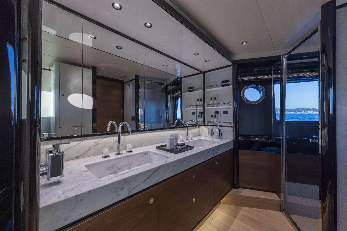 Modern yacht bathroom featuring a marble sink, mirrors, stylish taps, and a porthole with a sea view.